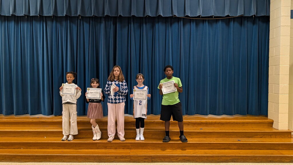 Five children stand on a stage with certificates, blue curtain backdrop, and a wooden floor.