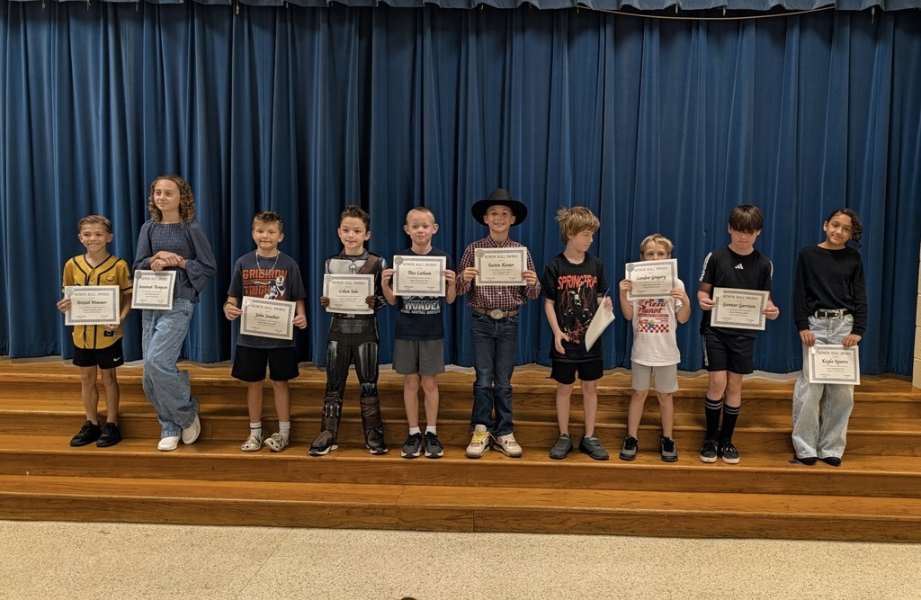 Kids on stage holding certificates, blue curtain in the background, standing on wooden steps.