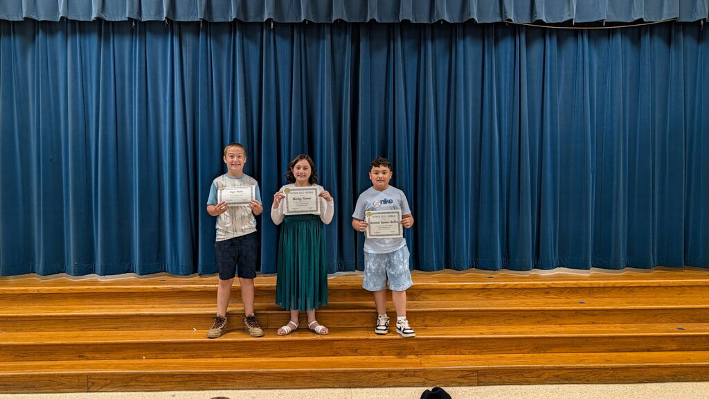 Three students stand on stage with certificates in hand in front of a blue curtain.