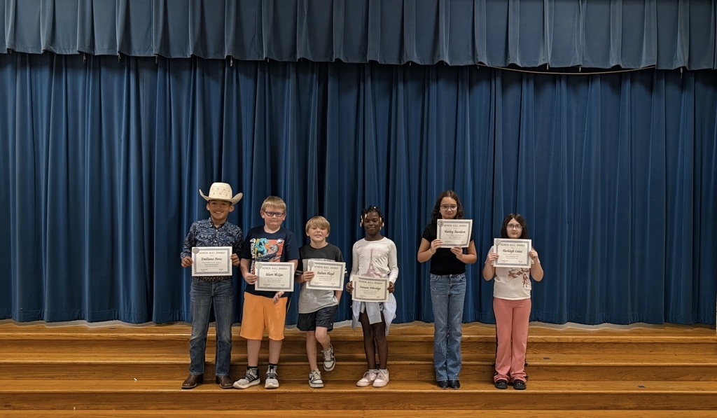 Seven children standing on a stage, each holding a certificate, blue curtain in the background.