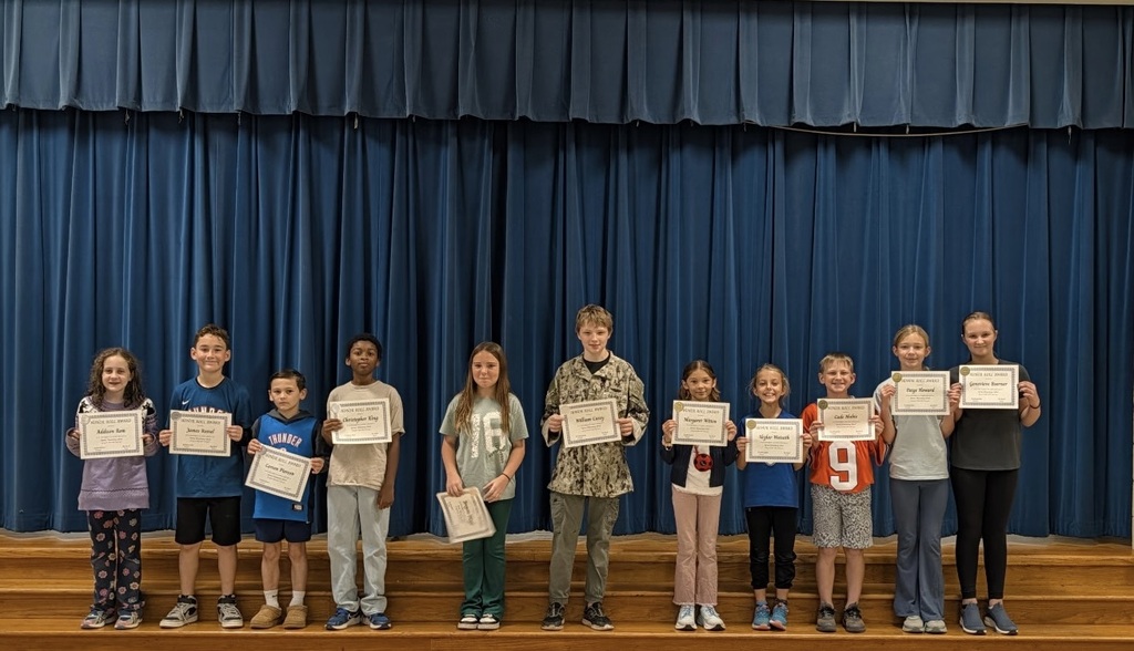 Students on stage with certificates, blue curtain in background.
