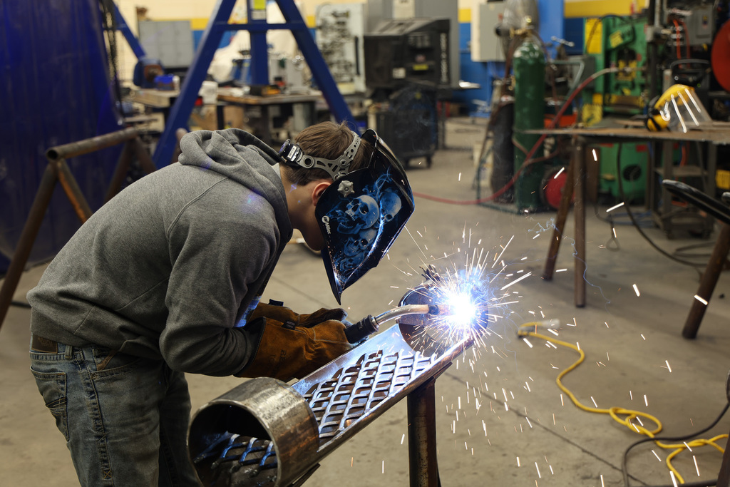 “Person wearing a welding helmet and gloves using a torch to weld metal in a workshop.”
