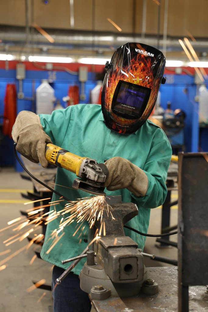 “Person wearing a welding helmet and protective gloves using a power grinder, with sparks flying in a workshop."