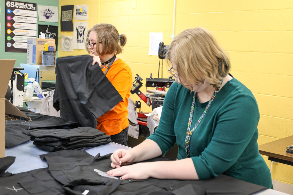 two students using chalk and marking shirts for embroidery