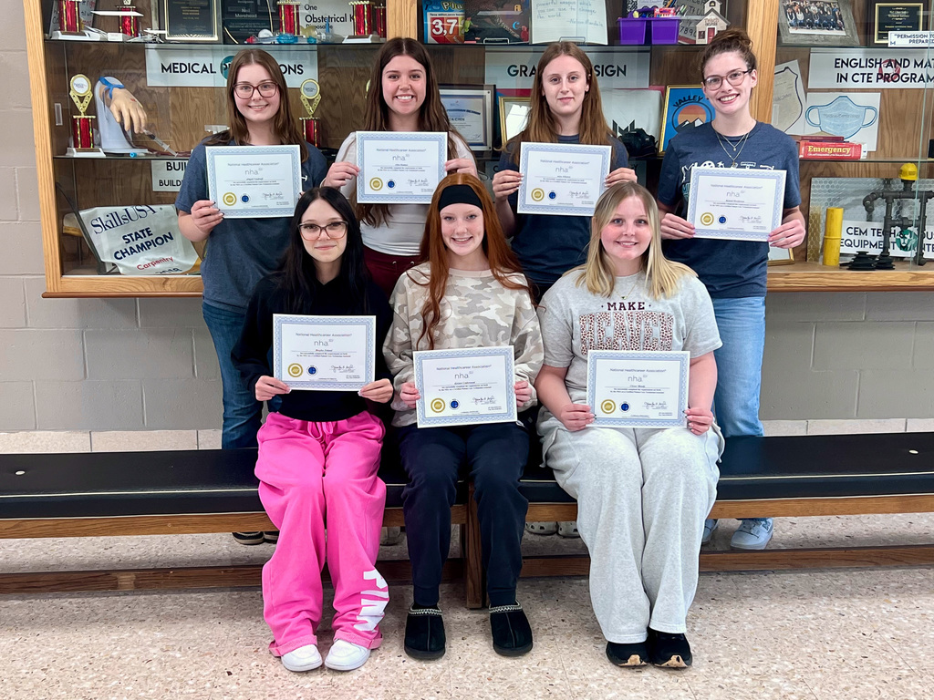 7 students smiling while holding certificates, in school lobby