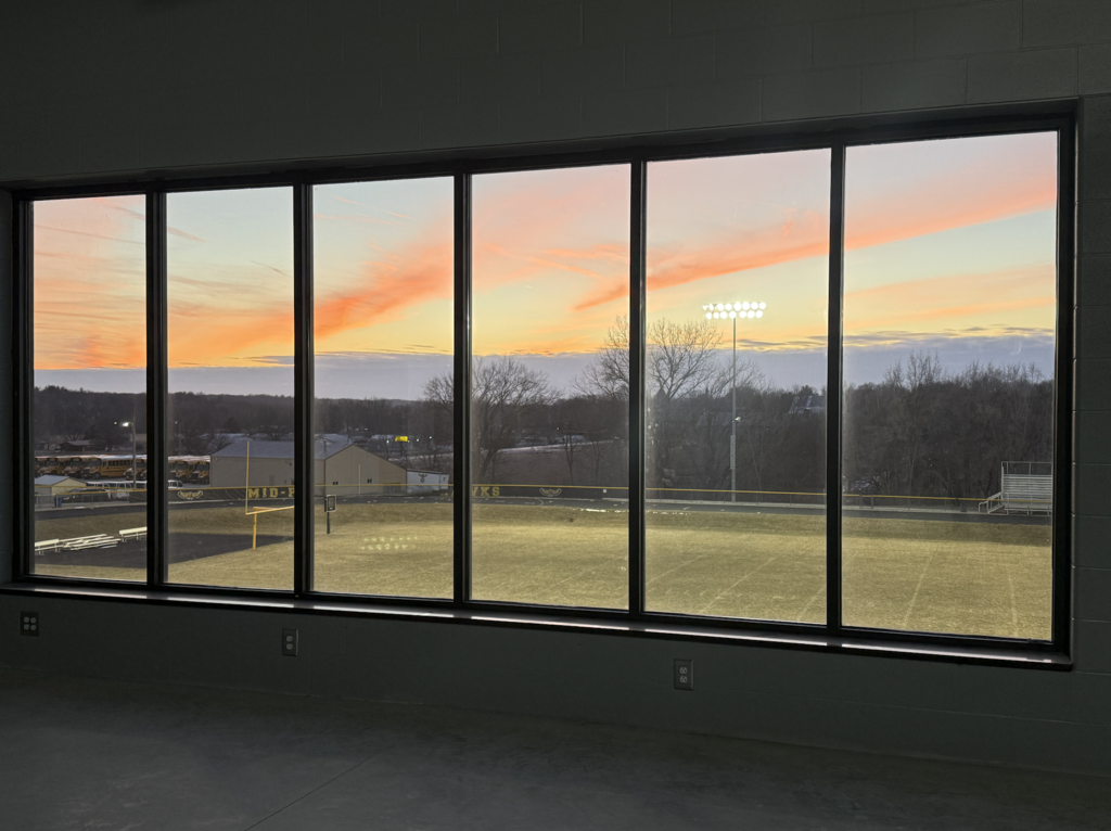 Looking out the large window of the activities building weight room over the MP football field with an Iowa sunset in the background