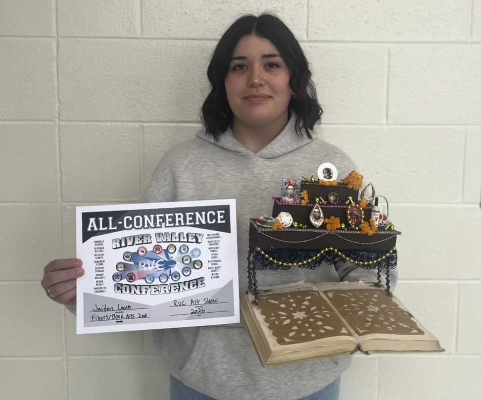 Student with artwork piece of a table with decorations on an open book and all-conference award