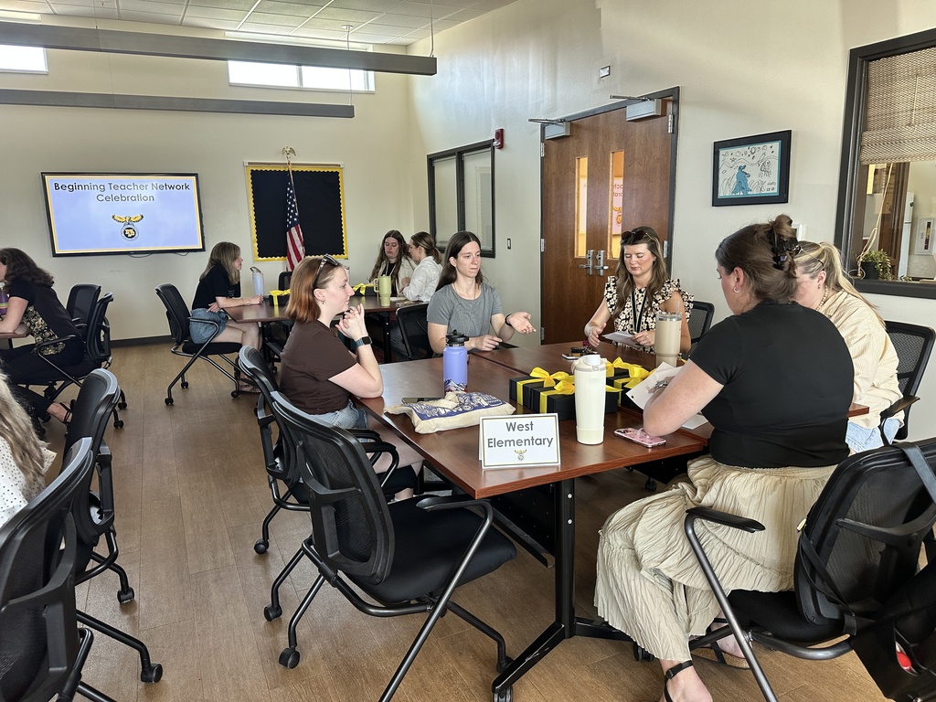 Teachers sitting in groups of 5 at tables in the MP Central Office community room talking to each other; Table sign reads West Elementary