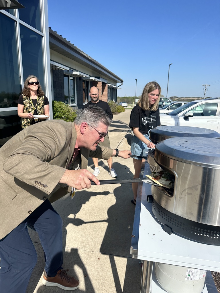 Superintendent Brian Stone cooking personal pizzas in his outdoor pizza ovens with three teachers standing to the side waiting
