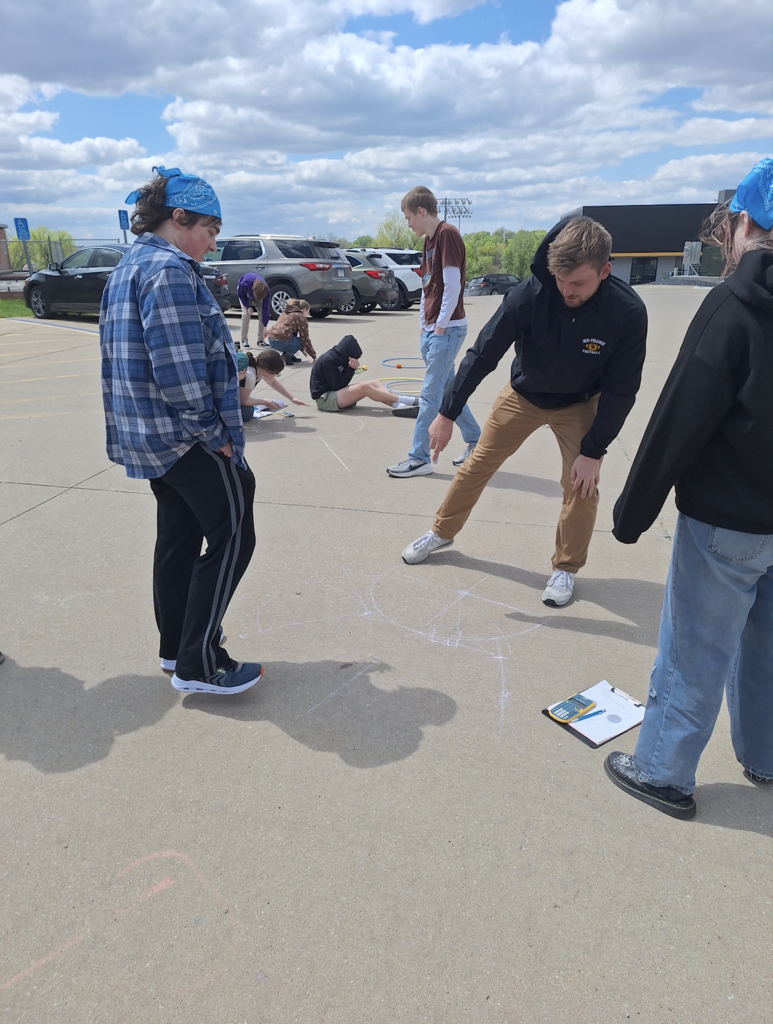 High school students pointing to circles drawn on the parking lot pavement with chalk discussing them