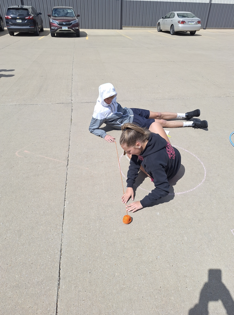 Male and female high school students drawing circles with chalk on the parking lot pavement