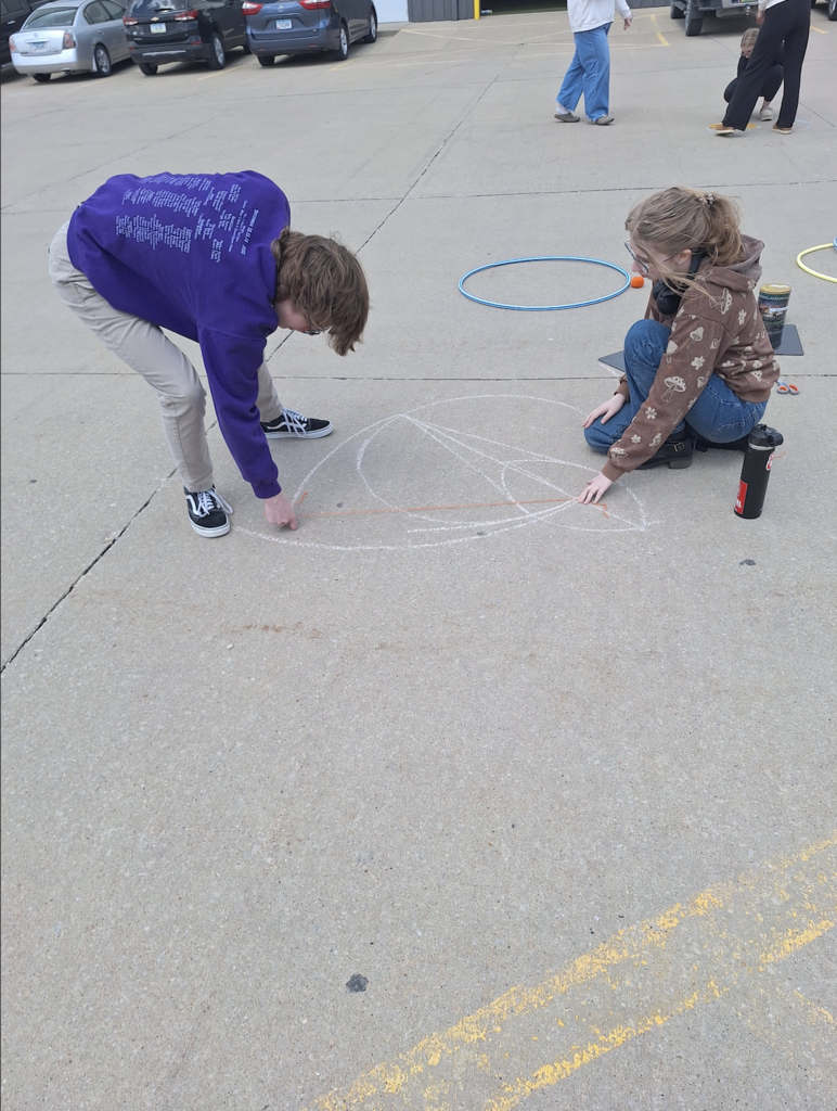 Male and female high school students drawing circles with chalk on the parking lot pavement