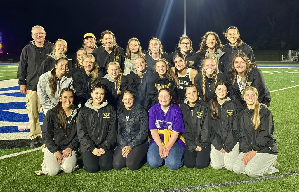 Girls track team members posing together with coaches on a field at night time under the lights