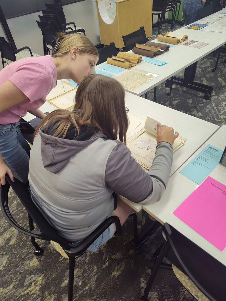 Students sitting at a table looking through books, papers and maps together