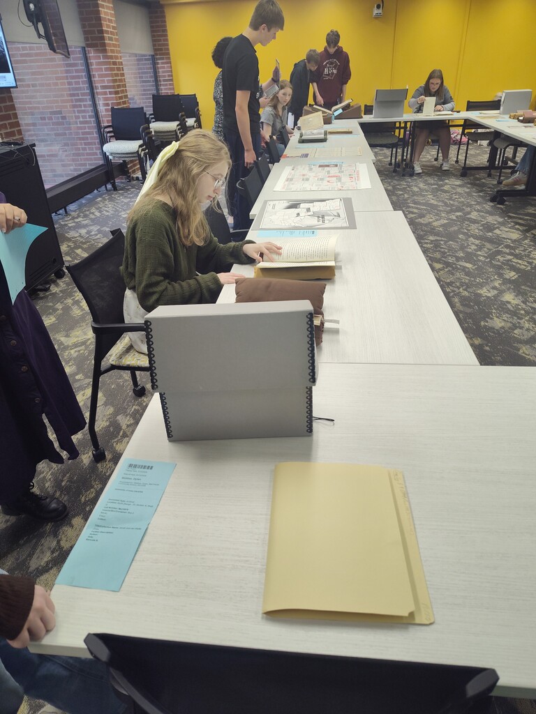Students sitting at a table looking through books, papers and maps together