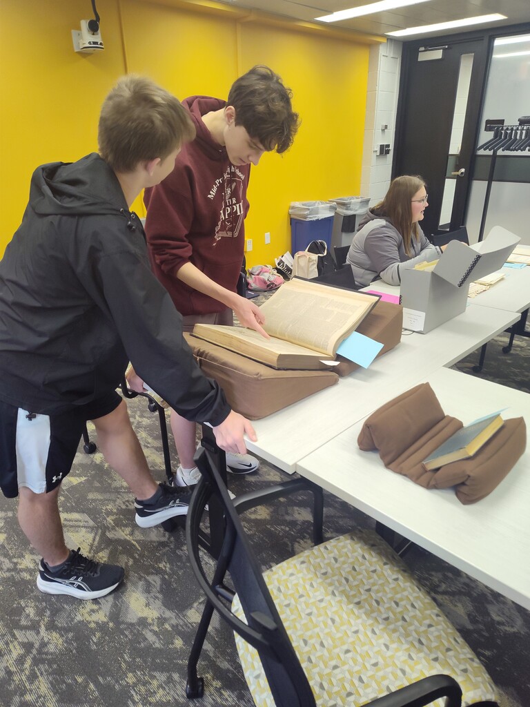 Students sitting at a table looking through books, papers and maps together