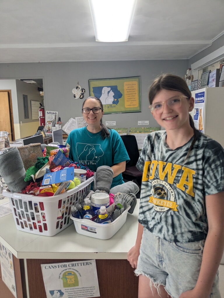 Jenna Puttmann and PAWS & More staff smiling with a laundry basket full of pet toys and supplies and another white tub of pet supplies