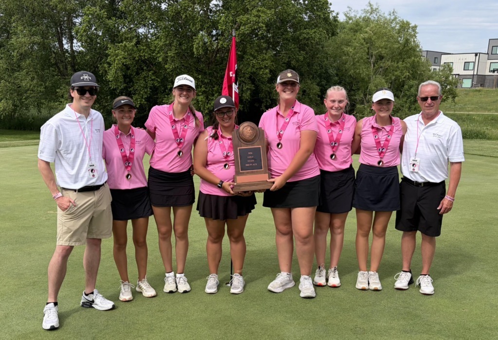 Girls golf team members wearing pink shirts and black skirts with coaches holding their 3rd place trophy