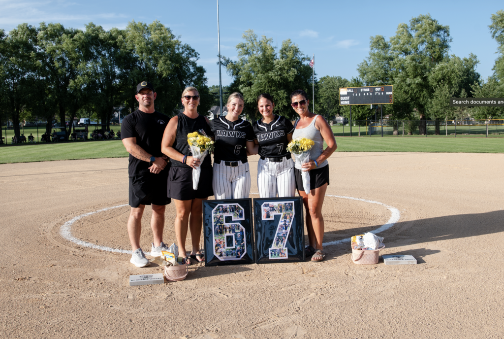 Kadence Grout and Sophie Miller with their families in softballu niforms with a 6 and 7 poster in front of them on the softball field