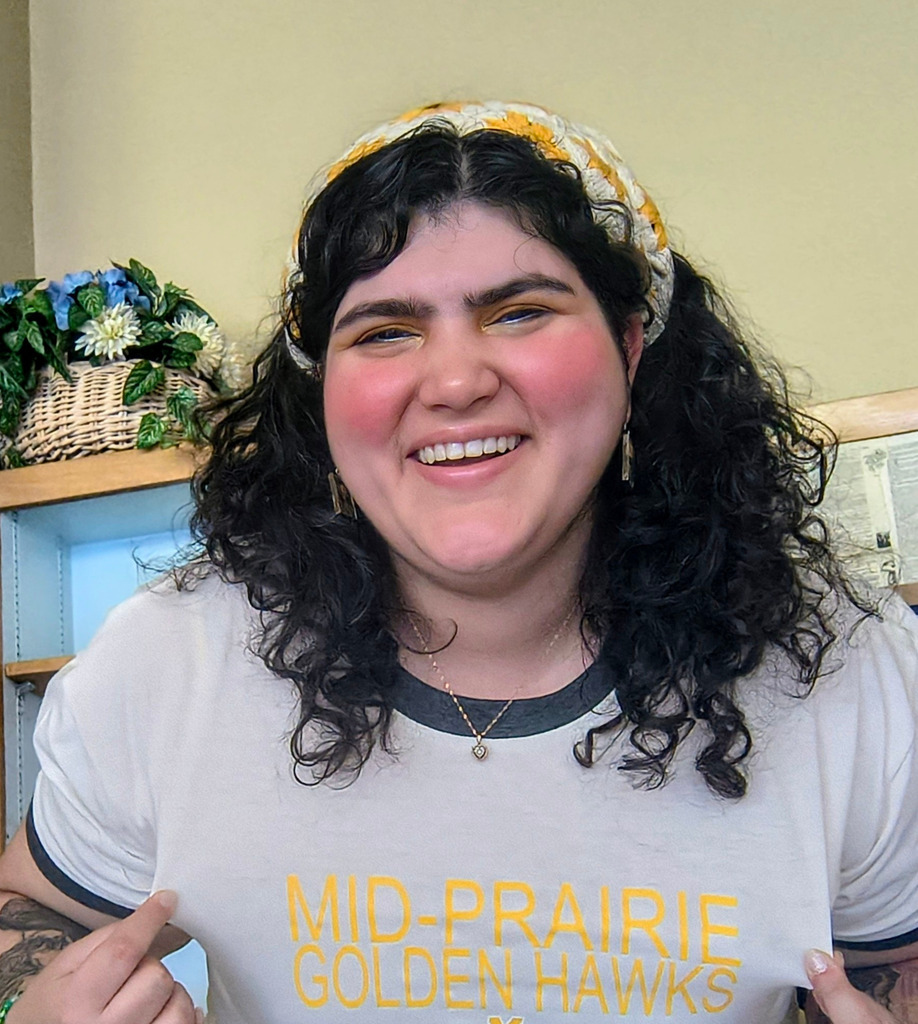 Emma Kossley smiling with a yellow headband and a shirt that reads Mid-Prairie Golden Hawks
