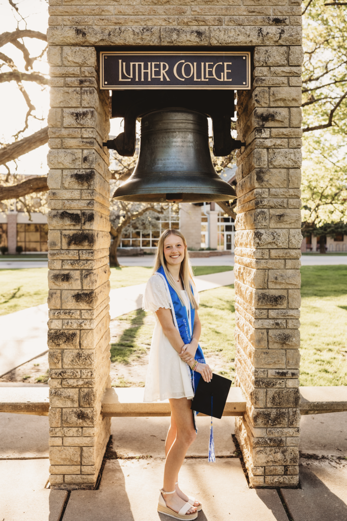 Teagan Schaefer standing in front of a stone structure and bell that says Luther College above it