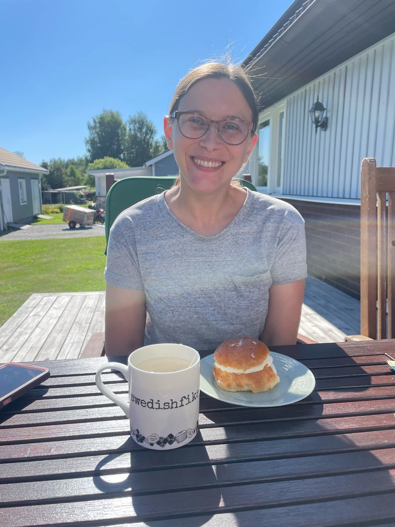 Gina Marner sitting at a table outdoors with a burger on her plate and a white coffee cup that says swedishfish