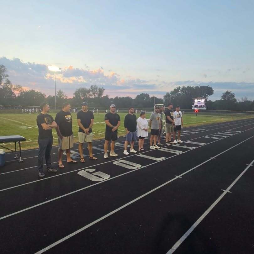 1976 Football team players standing on the track in front of a sunset over the football field