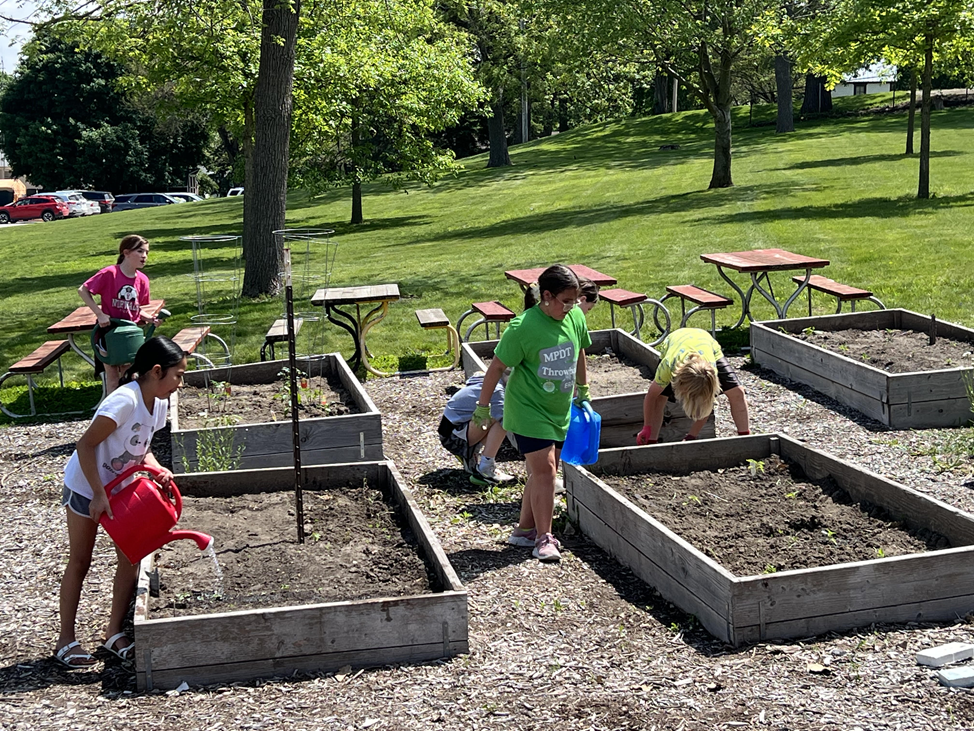 Students watering flowers and pulling weeds in the MP-West school garden