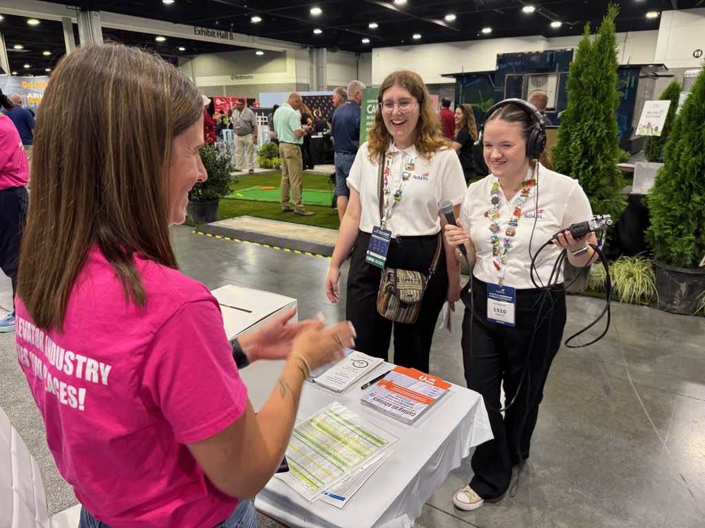 Two multimedia students working on audio exploring like convention center woman in pink shirts talking to them