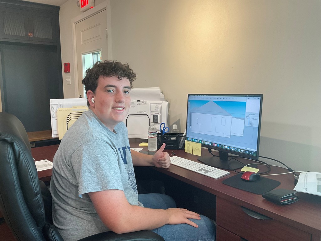 This is a picture of Brian in a blue shirt sitting at his desk thumbs up he's got a smile on his face