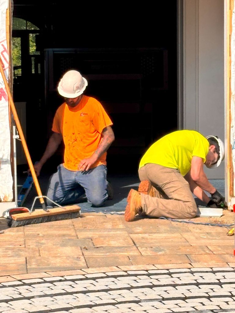 there's a picture of brian and jason they're working on some pavers both of them have white hard hats on jason has an orange shirt ryan has a yellow shirt