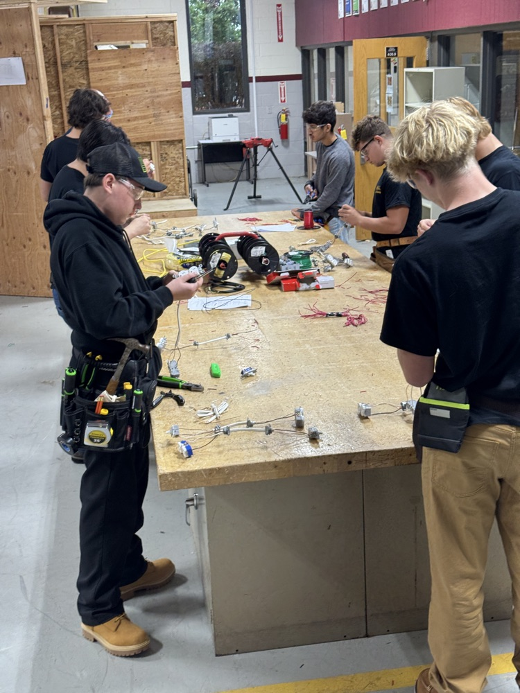 multiple electrical students with safety glasses on and their uniforms working on wiring at their workbenches