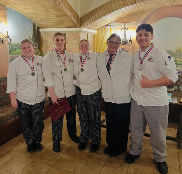 It's a group photo of the culinary art students and their whites with their medals around their neck in a restaurant