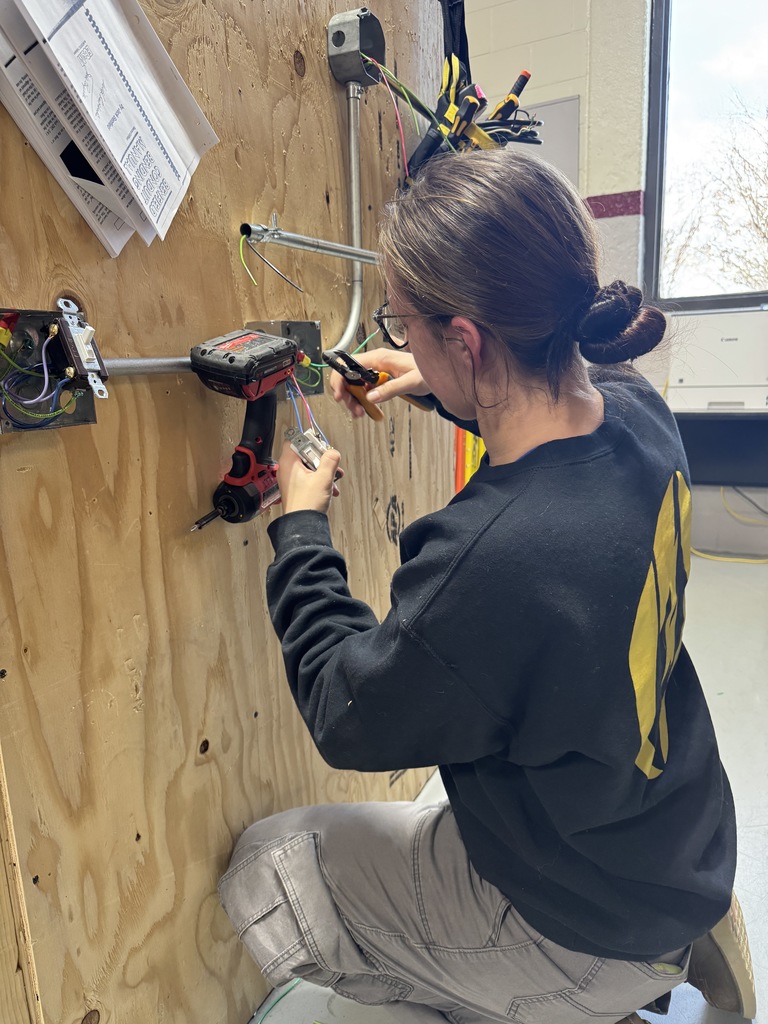 This is electrical student. She's got a black sweatshirt on her hair in a bun and she's working on some electrical panel.