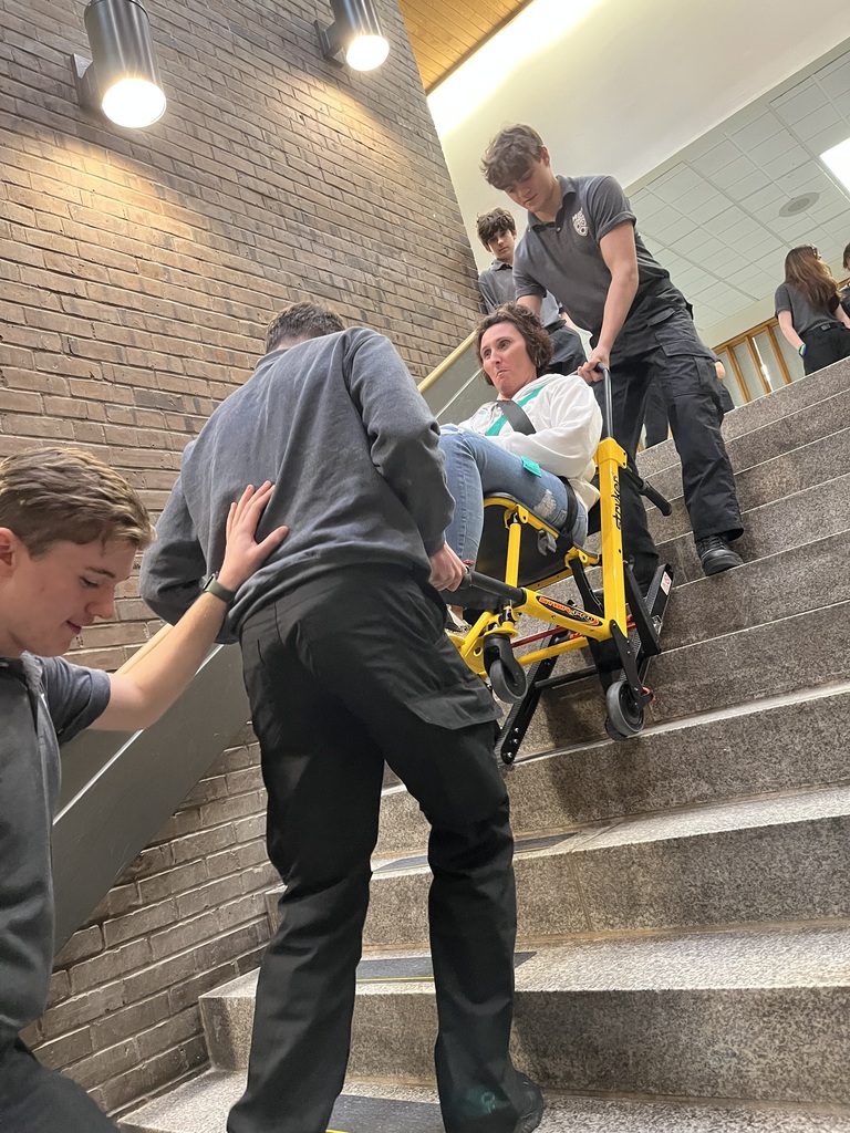 This photo is about several students that are on the stairs using what's called a stair climber. And their training. And there's a staff member in this Derek Climber. They're using it to bring her up and down the stairs.