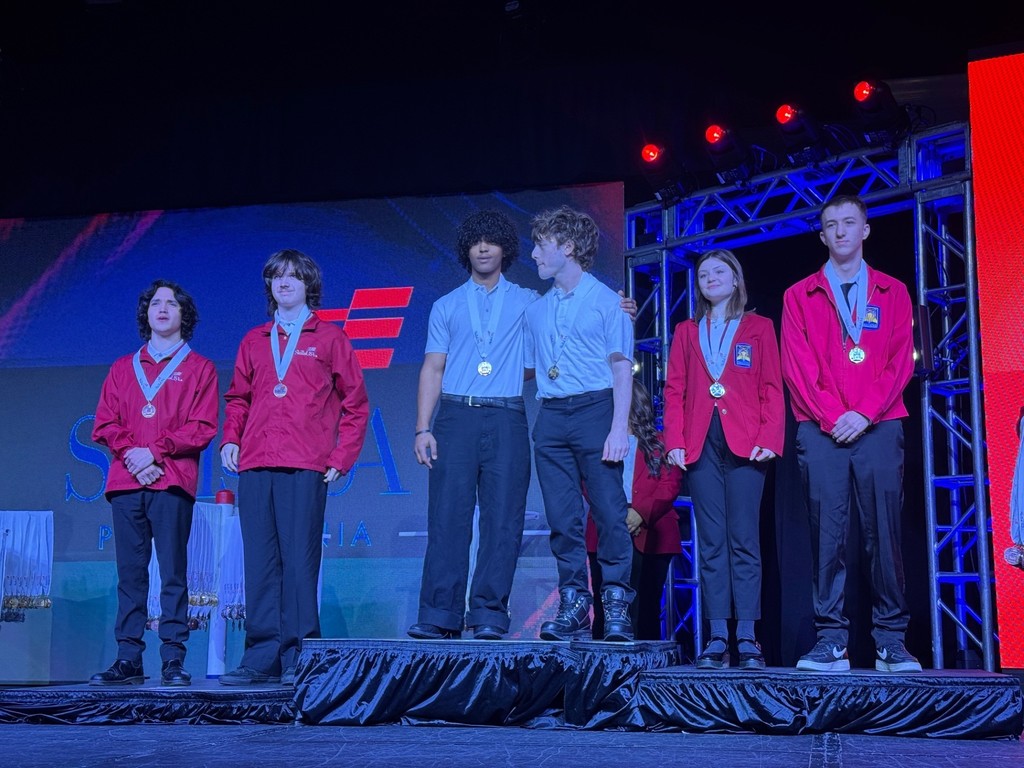 This picture on stage of the silver medal winners. They have the red jackets on and they're medals. With four other.