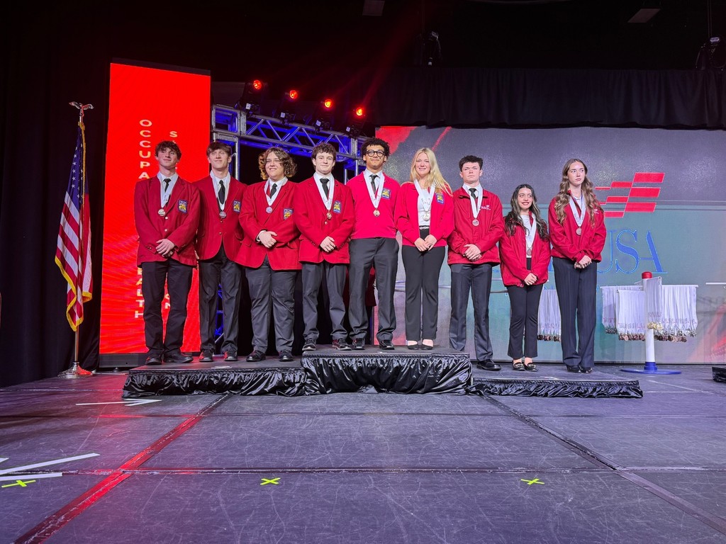 This is a picture of the stage with multiple winners, three of ours with their red jackets on and their gold medals