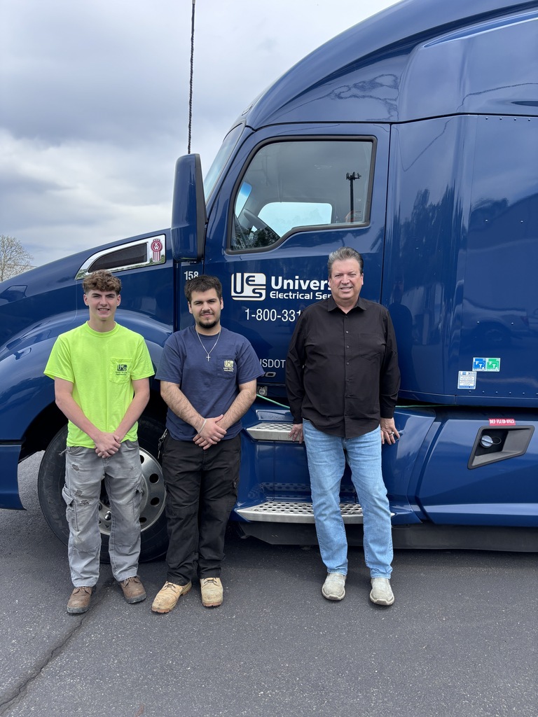 Three people standing two students and looks like his mentor or the owner next to a semi truck