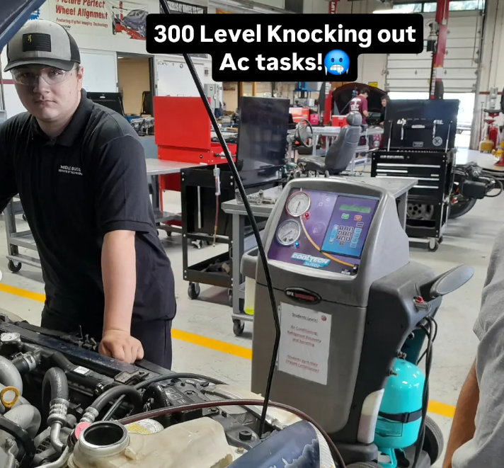 Working underneath the hood of a car in the automotive program