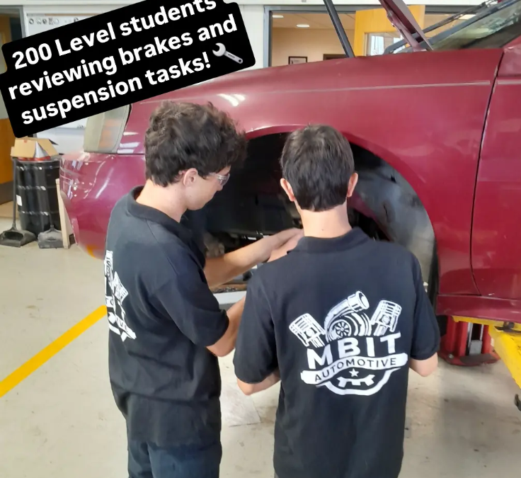 Student in the automotive program and their uniforms working on a car