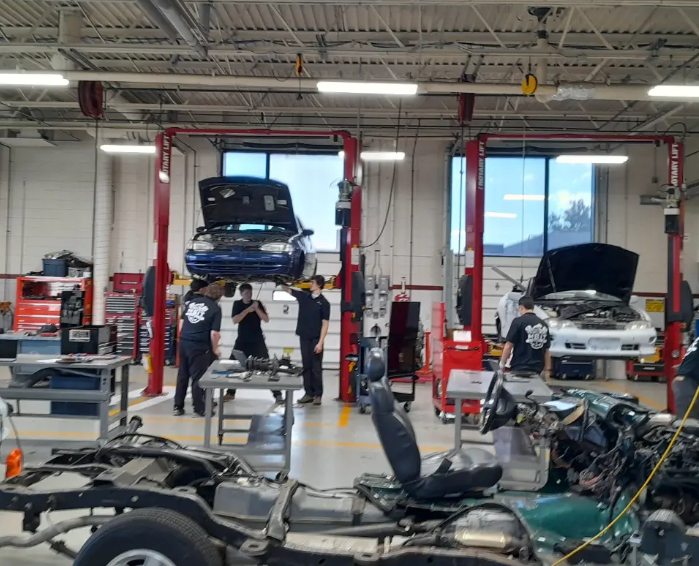 Large picture of the whole area with the students in the background working underneath the car