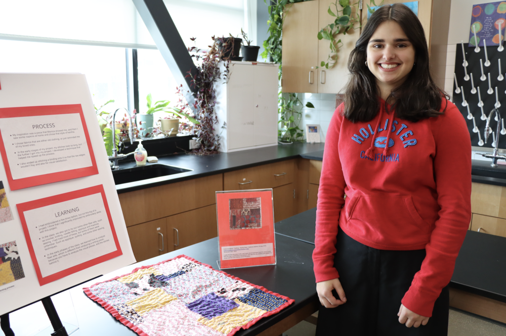Student smiling in front of embroidery project display