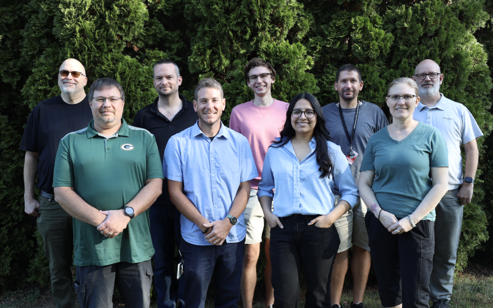 Technology Services team members smiling and standing in front of bushes