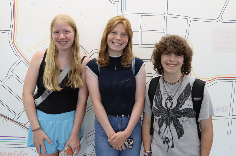 High school students smile and stand in front of a mural