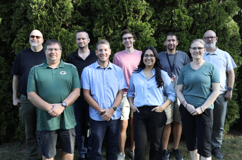 Members of the Technology Services team smiling and standing in front of trees