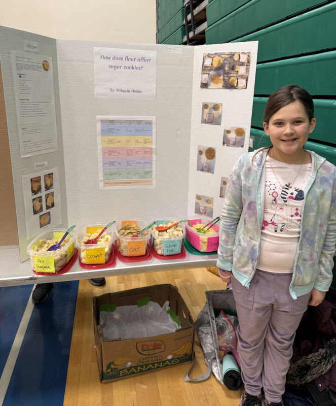 Student smiles in front of science project display at the Pope Farm Elementary School STEAM Fair