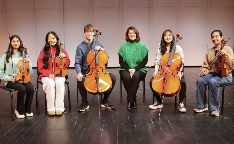 Diya Chilukuri, Vivian Feng, Kyle McIntosh, Dr. Dana Monogue, Hannah Lee, and Shaila Holland smiling. The students are holding their instruments.