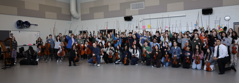 MHS Orchestra students and teacher Steve Kurr posing with instruments and smiling alongside Mark Wood and Jaylon Banks
