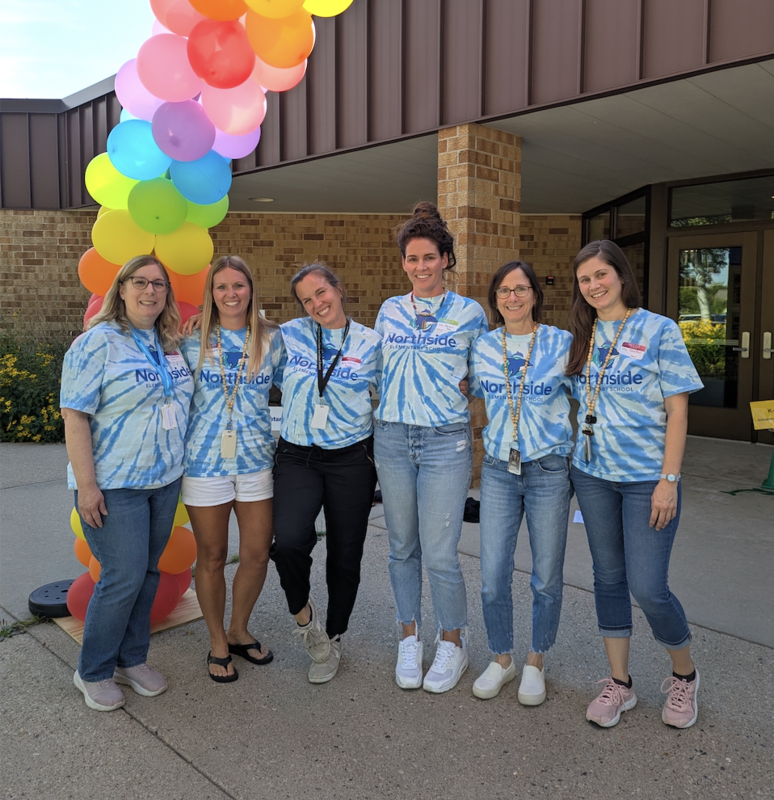 Northside Elementary School paraeducators standing under balloon arch and smiling