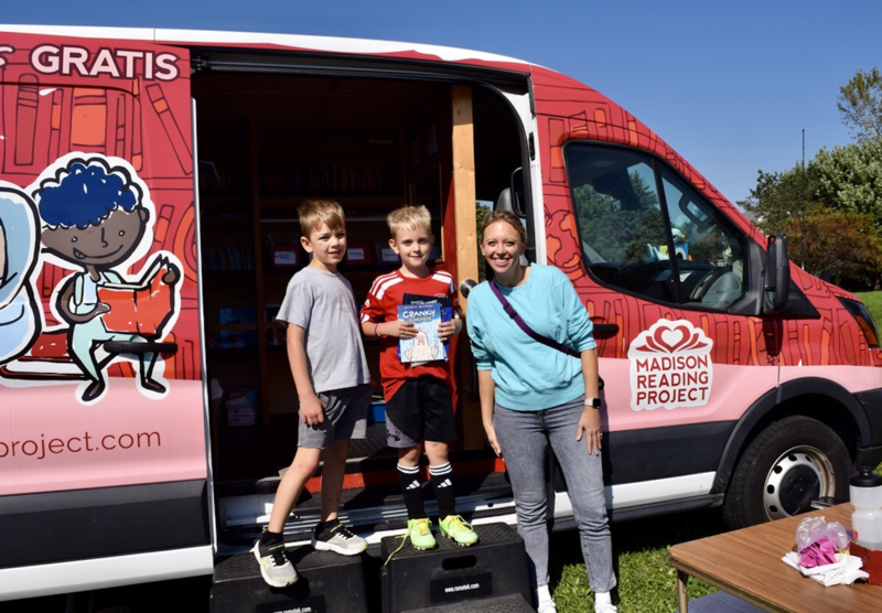 Parent and two children smiling while holding books by the Madison Reading Project bookmobile